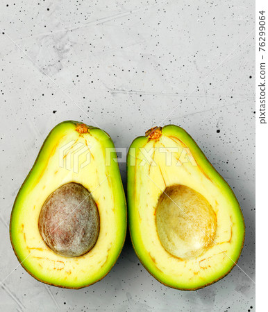 Avocado, cut in half, one slice with a core, on a gray concrete background, top view. Avocado, cut in half, one slice with a core, on a gray concrete background, top view. 76299064