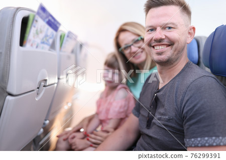 Smiling parents with child are sitting in aircraft cabin 76299391