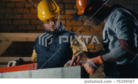 Multiracial builders measuring brick wall 76299567