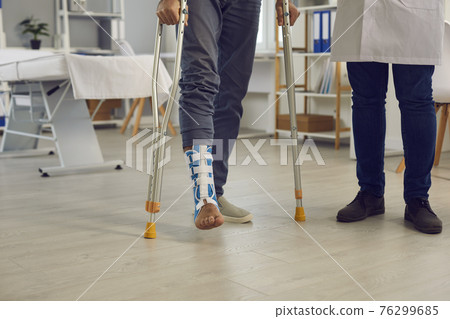 Midsection of patient with injured leg walk with crutches under doctor control 76299685