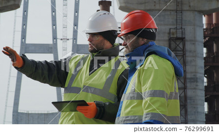 Male engineers discussing bridge drafts on tablet Male engineers discussing bridge drafts on tablet 76299691