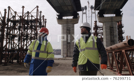 Male builders walking under bridge 76299731