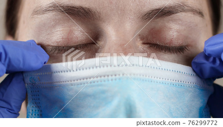 Young doctor or nurse with closed eyes in a protective medical mask, wearing latex medical surgical gloves 76299772