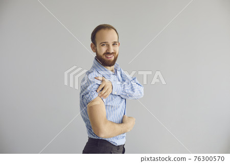 Portrait of happy young office worker smiling and showing his arm after getting vaccine 76300570
