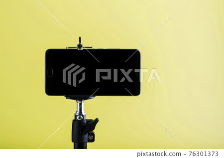 Smartphone attached to a tripod on a yellow background. Smartphone attached to a tripod on a yellow background. 76301373