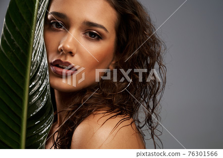 Woman behind big green leaf, isolated on gray. 76301566