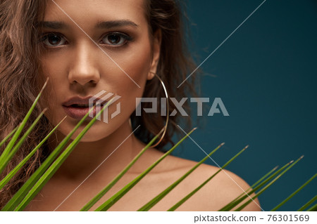 Woman behind palm leaf, isolated on blue. 76301569