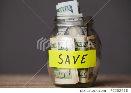 Dollar bills in glass jar and text save on wooden table 76302418