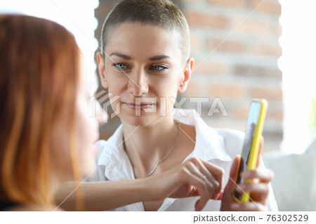 Smiling caucasian woman holding mobile phone talking with friend Smiling caucasian woman holding mobile phone talking with friend 76302529
