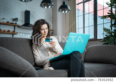 young female make online purchase with credit card and laptop on sofa at home young female make online purchase with credit card and laptop on sofa at home 76302692