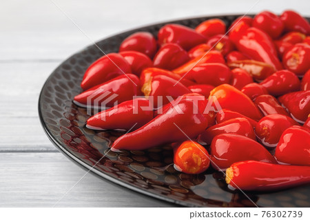 Close-up of pickled baby red hot peppers on a black plate. Close-up of pickled baby red hot peppers on a black plate. 76302739