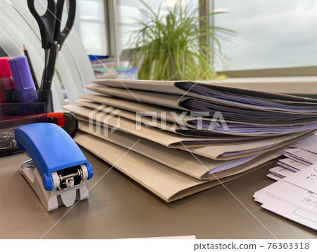 Large thick folders with important papers and documents on a working office desk with stationery and accessories Large thick folders with important papers and documents on a working office desk with stationery and accessories 76303318