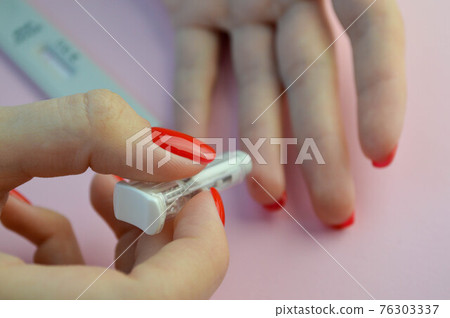 coronavirus test on a pink matte background. medical procedure. girl with bright red nails makes an analysis and pierces her finger with a lancet 76303337