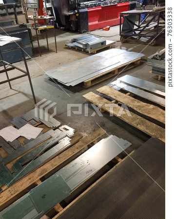 Metal blanks and parts made of galvanized steel sheets lie on wooden pallets at a metalworking plant 76303338