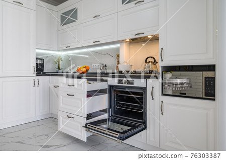 Luxurious white modern kitchen interior, drawers pulled out, oven's door open 76303387
