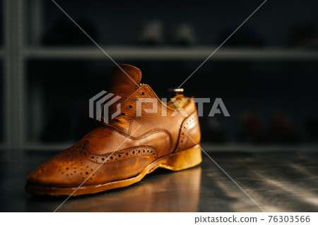 Close-up side view of old light brown leather shoes with wooden shoe pad to be repaired in dark craft shoe shop. 76303566