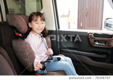 A girl wearing a seatbelt with a junior seat attached to the passenger seat 76306797