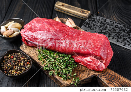 Raw Tenderloin veal meat for steaks fillet mignon on a wooden cutting board with butcher cleaver. Black wooden background. Top view Raw Tenderloin veal meat for steaks fillet mignon on a wooden cutting board with butcher cleaver. Black wooden background. Top view 76307682