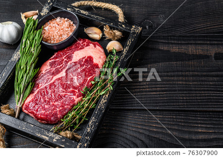 Raw prime rib eye beef meat steak in a butcher wooden tray with herbs. Black wooden background. Top view. Copy space Raw prime rib eye beef meat steak in a butcher wooden tray with herbs. Black wooden background. Top view. Copy space 76307900