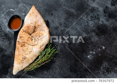 Calzone closed pizza with ham and cheese. Black background. Top view. Copy space Calzone closed pizza with ham and cheese. Black background. Top view. Copy space 76307972