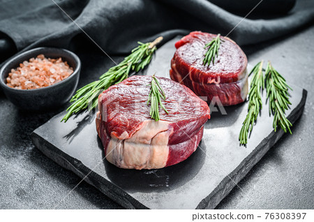 Two pieces of thin steak cut from the tenderloin. Black background. Top view. Two pieces of thin steak cut from the tenderloin. Black background. Top view. 76308397