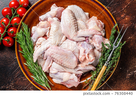 Cut Raw chicken wings in a rustic plate with thyme and rosemary. Dark background. Top view 76308440