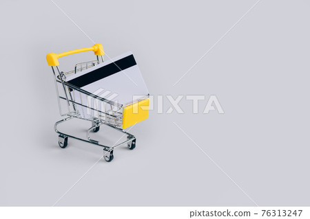 Yellow shopping cart with credit card inside on light gray background with copy space for text. Sale event, Black Friday and Cyber Monday concept in colors of the year 2021. Selective focus 76313247