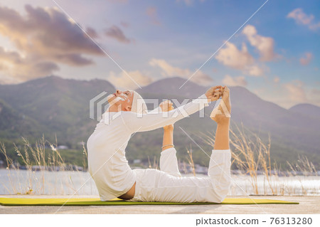 Kundalini yoga woman in white clothes and turban practices yoga kundalini on the background of the sea, mountains and sunset. Fighting face painting of the Indians shows her inner world. Visual Kundalini yoga woman in white clothes and turban practices yoga kundalini on the background of the sea, mountains and sunset. Fighting face painting of the Indians shows her inner world. Visual 76313280