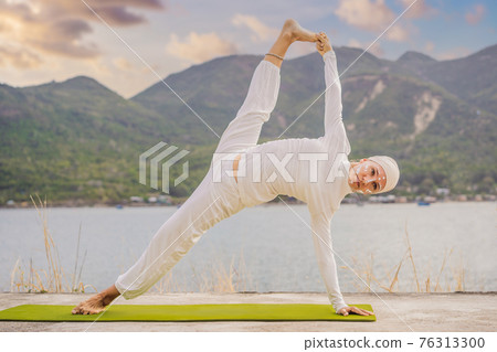 Kundalini yoga woman in white clothes and turban practices yoga kundalini on the background of the sea, mountains and sunset. Fighting face painting of the Indians shows her inner world. Visual 76313300