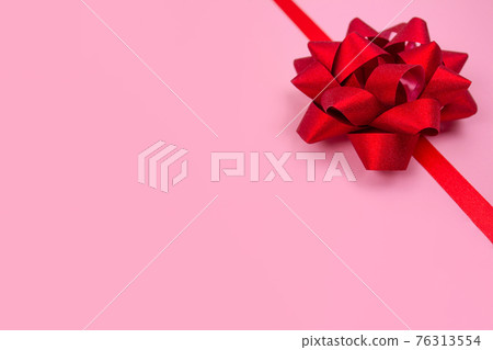 Decorative red ribbon bow on pink background with copy space for text. Giving presents concept. Greeting card or holidays sale background. Selective focus 76313554