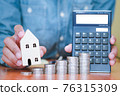 Both hands were holding a house and a calculator, and coins stacked in front of. 76315309