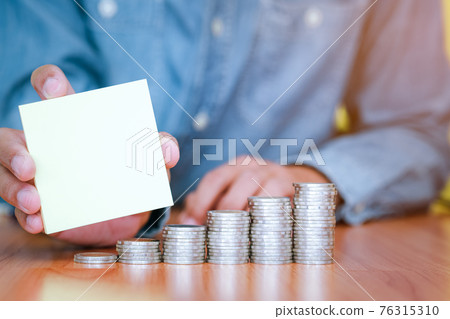 A businessman holding a blank note with coins stack placed on the front 76315310