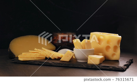 Several types of yellow cheese on black stone board. 76315671