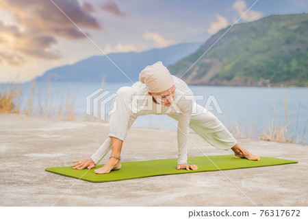 Kundalini yoga woman in white clothes and turban practices yoga kundalini on the background of the sea, mountains and sunset. Fighting face painting of the Indians shows her inner world. Visual 76317672