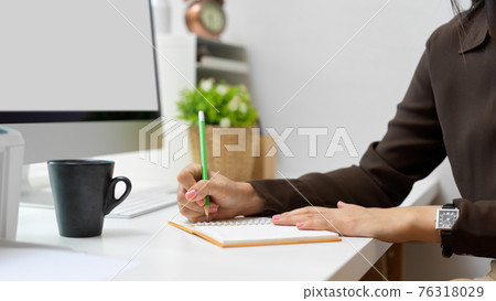 Side view of female hand writing on notebook on computer table Side view of female hand writing on notebook on computer table 76318029