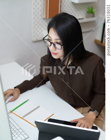 Female office worker concentrating on her work with computer and office supplies Female office worker concentrating on her work with computer and office supplies 76318031