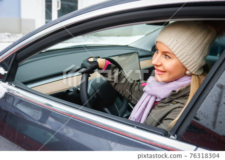 MINSK. BELARUS - JANUARY 2021: A beautiful woman looks out the window of an electric car. MINSK. BELARUS - JANUARY 2021: A beautiful woman looks out the window of an electric car. 76318304