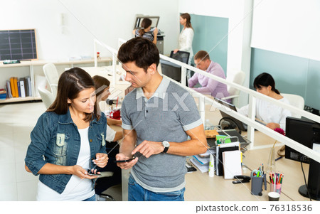 Male and female office co-workers having conversation at desk in office 76318536