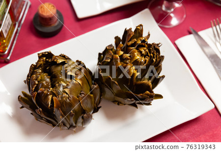 Vegetarian appetizer of baked artichokes served on white plate. 76319343