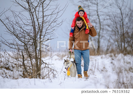 Winter walk, father with daughter and dog in the woods, bright winter clothes. Winter walk, father with daughter and dog in the woods, bright winter clothes. 76319382