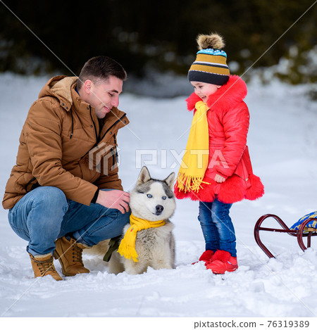 Happy father with daughter on a walk in the woods, girl and husky in yellow scarves, bright clothes in winter. Happy father with daughter on a walk in the woods, girl and husky in yellow scarves, bright clothes in winter. 76319389