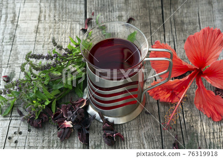 Glass cup of  red herbal Hibiscus tea with ingredients  on wooden table  against a blurred green meadow 76319918