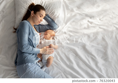 Co-sleeping with baby. Young woman napping in bed with her newborn child 76320043