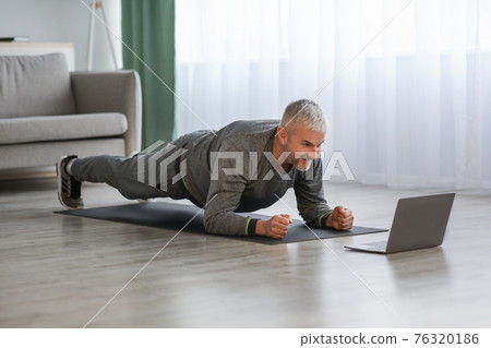 Athletic mature bearded man doing exercises at home, using laptop Athletic mature bearded man doing exercises at home, using laptop 76320186