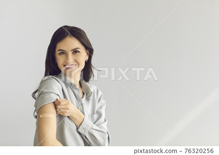Young woman on copy space background smiling and showing arm after vaccine injection 76320256