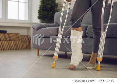 Woman standing with metal medical elbow crutches and showing broken injured leg 76320259