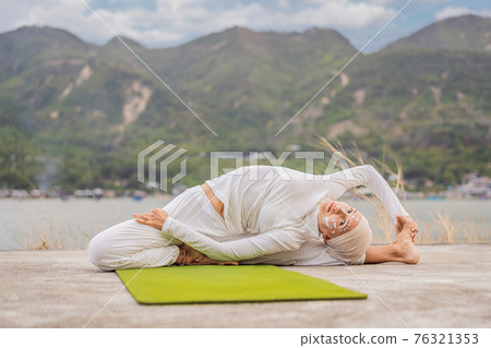 Kundalini yoga woman in white clothes and turban practices yoga kundalini on the background of the sea, mountains and sunset. Fighting face painting of the Indians shows her inner world. Visual Kundalini yoga woman in white clothes and turban practices yoga kundalini on the background of the sea, mountains and sunset. Fighting face painting of the Indians shows her inner world. Visual 76321353