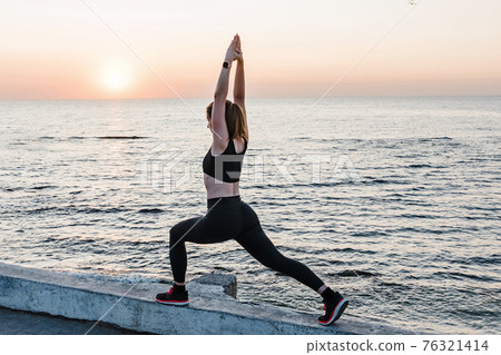 Young woman doing yoga or making exercises near the sea at sunrise. Young woman doing yoga or making exercises near the sea at sunrise. 76321414