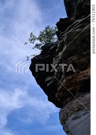 Rocky ledge with tree against the blue sky with clouds Rocky ledge with tree against the blue sky with clouds 76321903