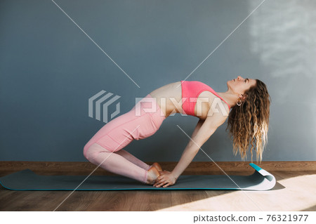 A young woman in sportswear practices yoga and performs asanas in a yoga class or at home. Yoga, sports, fitness. The concept of mental health and healthy lifestyle A young woman in sportswear practices yoga and performs asanas in a yoga class or at home. Yoga, sports, fitness. The concept of mental health and healthy lifestyle 76321977